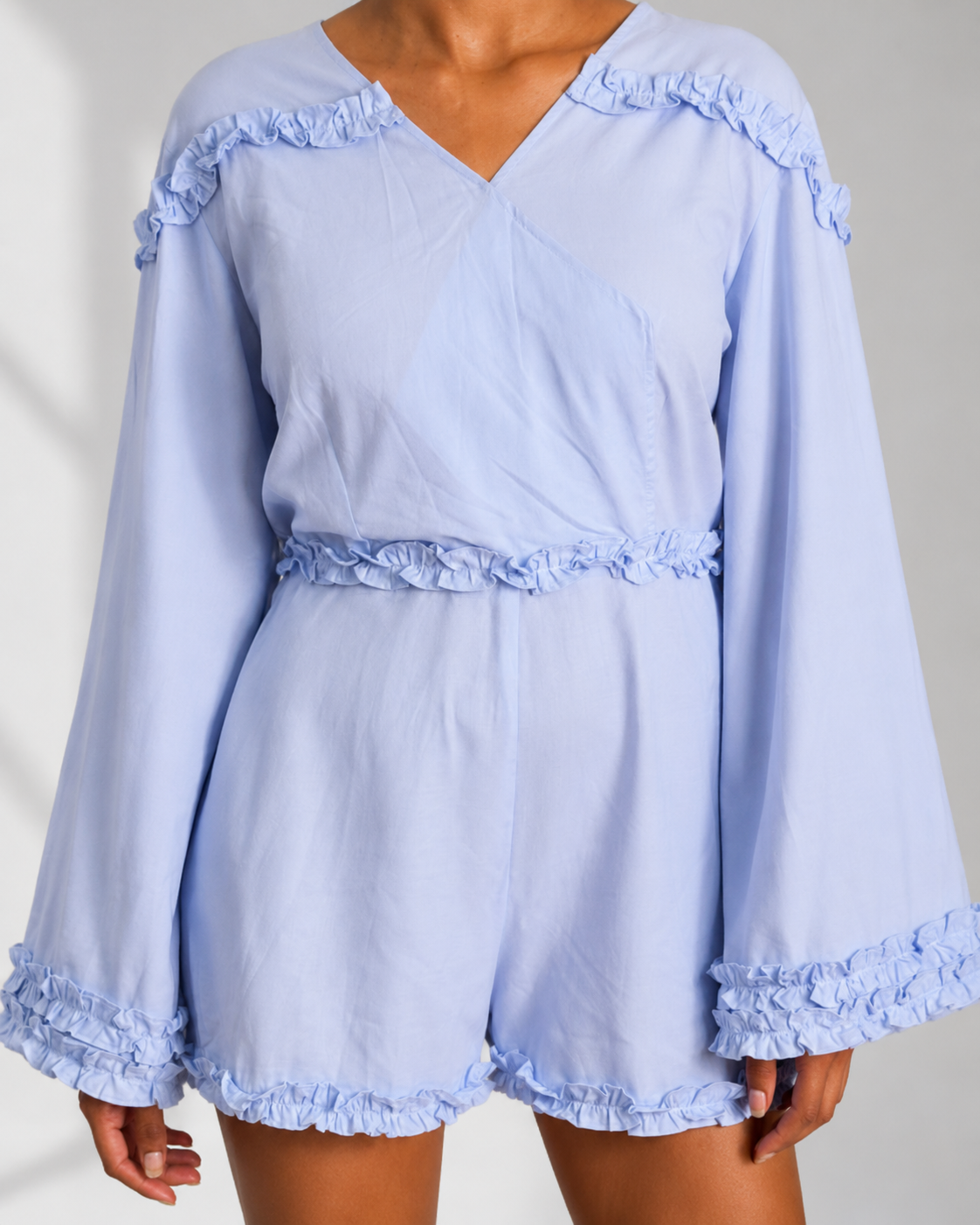Close view of the wrap V neckline and ruffle trims on the ISAURE powder blue playsuit.