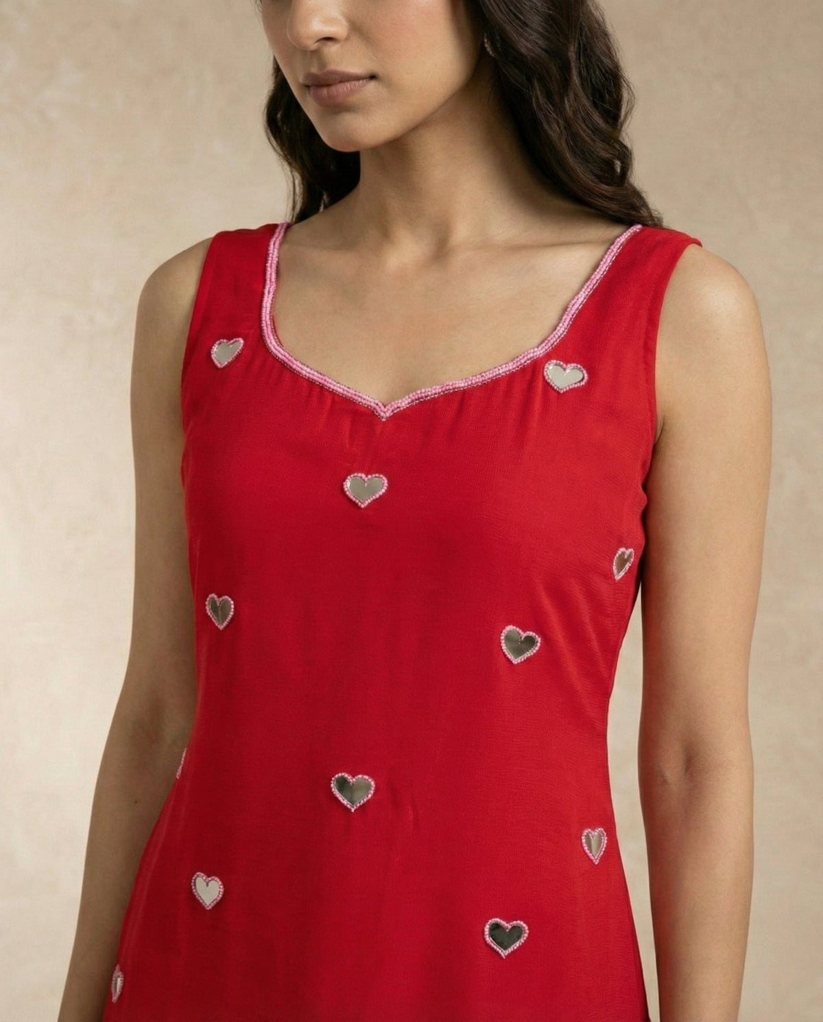 Close view of SANA's heart-shaped mirror motifs and embroidered sweetheart neckline on red.