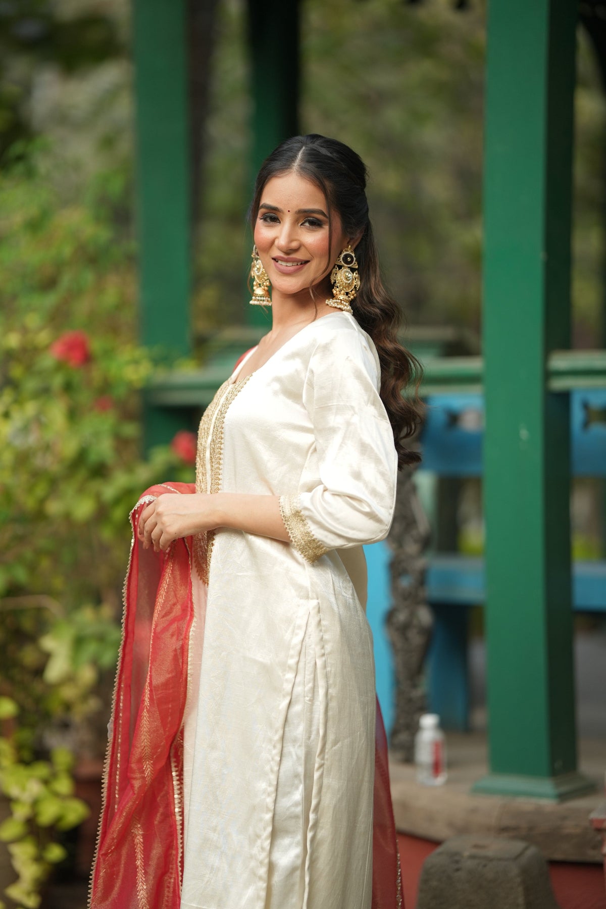 Off white silk kurta set with gold lace hem borders and a draped vermilion dupatta.