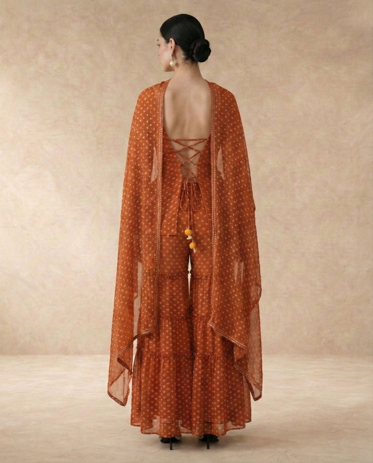 Back view of AMBER rust sharara set with criss-cross lace-up doori back and yellow pom-pom ties.