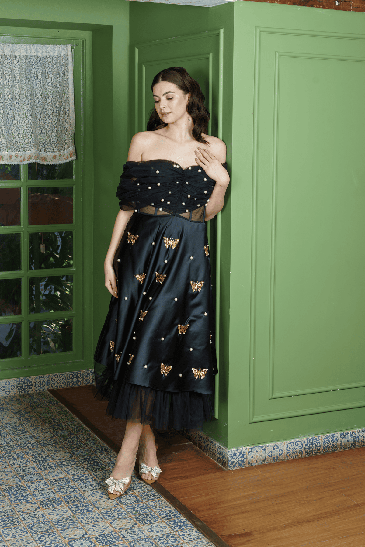 Model in Midnight Siren black off-shoulder dress with gold metal butterfly and pearl details